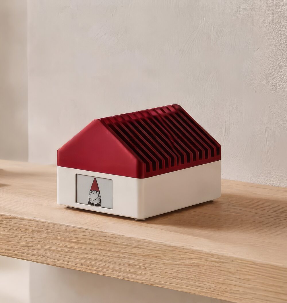 Tomte Tom, a small house-shaped device with a red gable roof, sitting on a wooden shelf.